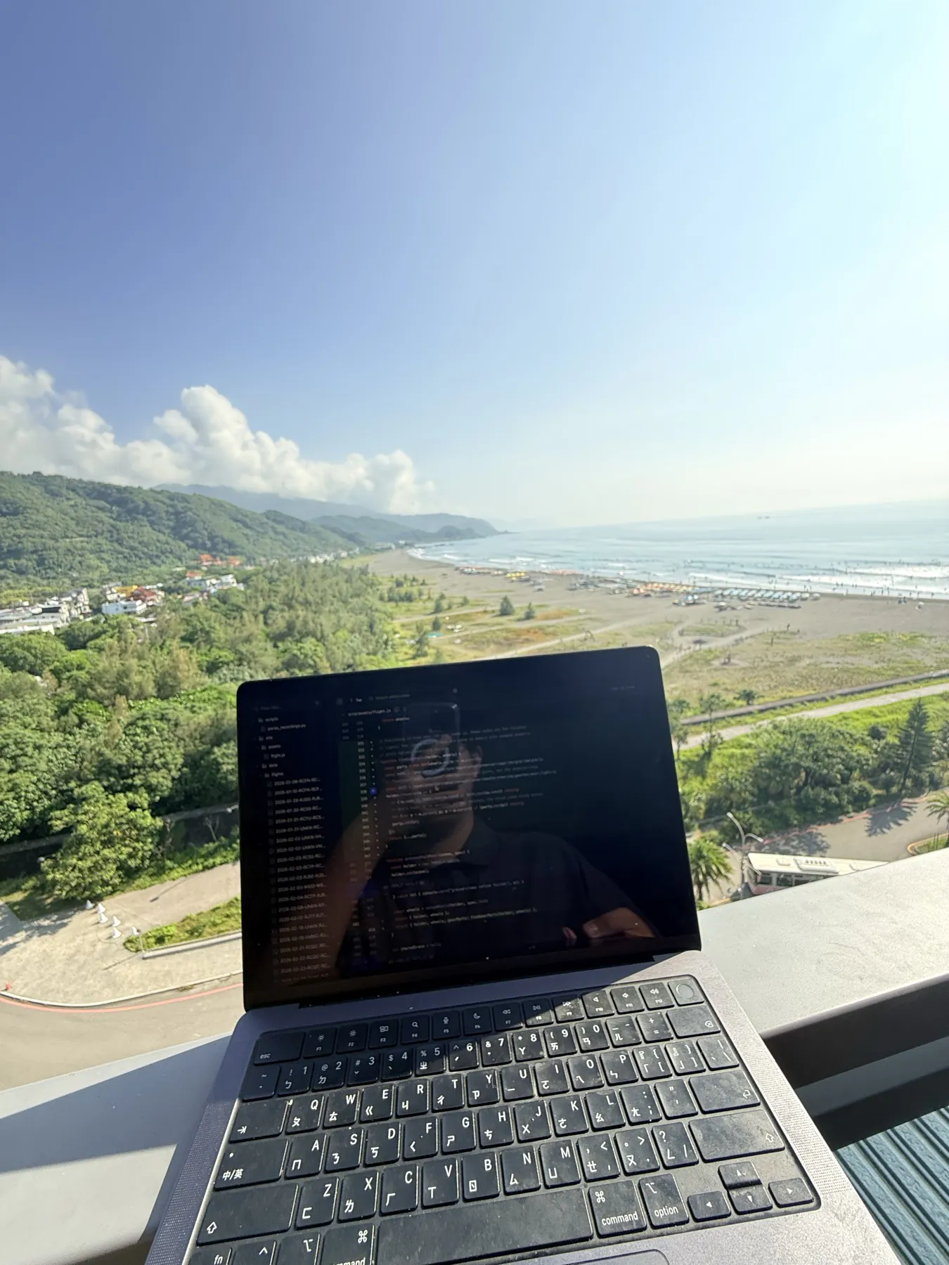 在 OA HOTEL 陽台檢查 GitHub，遠方為外澳沙灘上的衝浪人群